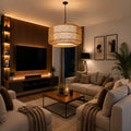 A modern living room featuring a large cylindrical woven rattan pendant light hanging above a wooden coffee table. The room is styled with beige sofas, a dark wood slatted TV wall with built-in shelves and warm lighting, and a potted palm plant.