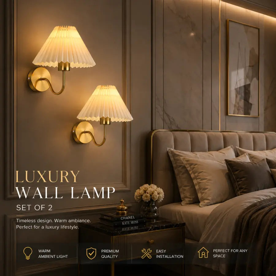 Two luxury wall lamps with pleated cream shades and gold fixtures mounted on a dark paneled wall above a bed in a styled bedroom setting.