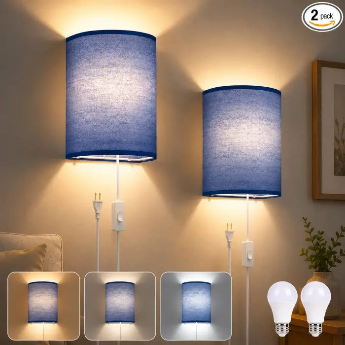 Two blue fabric drum pendant lights with white cords and switches, shown lit in a bedroom setting. The image includes three inset views at the bottom showing the light color under warm and cool lighting, and two clear light bulbs at the bottom right, with a '2 pack' badge in the top right corner.
