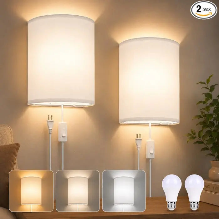 Two white drum-shaped wall sconces with cord and plug controls, shown lit on a beige wall above a wooden surface. A small inset row shows different light colors, and two loose bulb bulbs are shown at bottom right.
