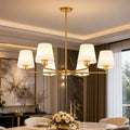 A modern six-light brass chandelier with white drum shades hangs over a dining table in a stylishly decorated dining room.
