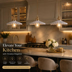 Three vintage-style pendant lights with scalloped white glass shades and warm brass hardware hang over a modern kitchen island. The scene includes marble countertops, dark cabinetry, a marble backsplash, and decorative flowers on a tray, with promotional text overlaid on the left side.