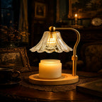 A vintage-style table lamp with a clear ribbed glass bell shade, a curved brass arm, and a warm white candle jar on a round wooden base, placed on a dark wooden table in a dimly lit room.