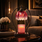 A decorative table lamp with a pink glass shade and a lit pink candle holder base, displayed on a dark marble table in a cozy living room setting.