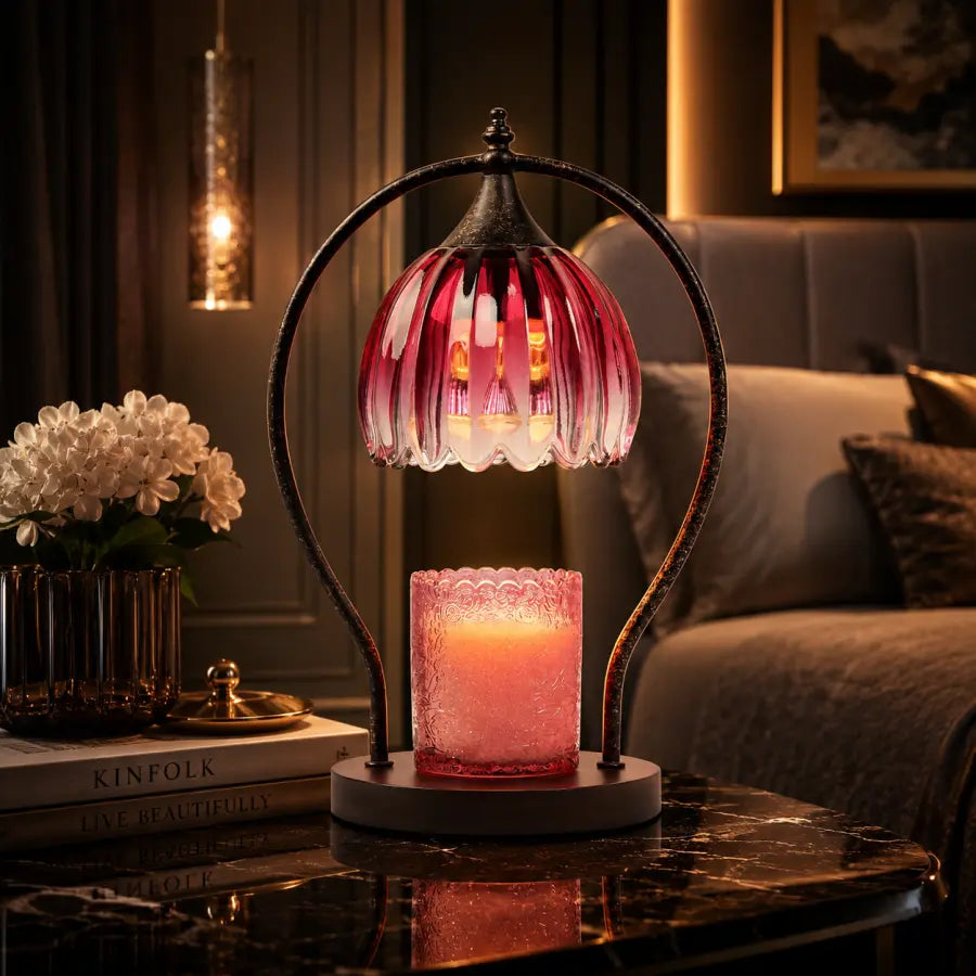 A decorative table lamp with a pink glass shade and a lit pink candle holder base, displayed on a dark marble table in a cozy living room setting.