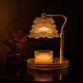 A warm amber table lamp with a tiered crystal shade and a matching crystal candle holder on a round base, set on a dark reflective surface with a small vase of dried stems beside it.