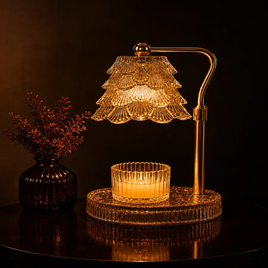 A warm amber table lamp with a tiered crystal shade and a matching crystal candle holder on a round base, set on a dark reflective surface with a small vase of dried stems beside it.