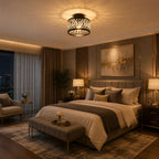 A modern bedroom featuring a decorative black metal ceiling light with a glowing warm light, styled with beige and brown bedding, a matching upholstered bench, and a city view window in the background.
