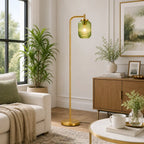 A modern floor lamp with a gold-finished metal stand and a ribbed translucent green glass shade, glowing with a warm light in a styled living room.