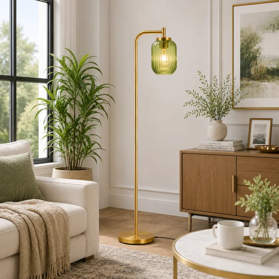A modern floor lamp with a gold-finished metal stand and a ribbed translucent green glass shade, glowing with a warm light in a styled living room.