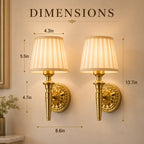 Two gold wall sconces with pleated cream shades shown on a beige wall with overlaid dimension labels and the word DIMENSIONS at the top.