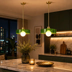Two modern pendant lights with green glass shades and brass hardware hang over a marble kitchen island in a contemporary kitchen setting.