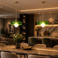 Two modern pendant lights with translucent green glass shades and gold-toned hardware hang over a dining table in a stylishly lit contemporary kitchen and dining space.
