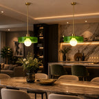 Two modern pendant lights with translucent green glass shades and gold-toned hardware hang over a dining table in a stylishly lit contemporary kitchen and dining space.