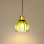A hanging pendant light with a ribbed translucent yellow-green glass shade, a brass-toned metal cap, and a black cord against a warm beige background.