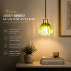 A modern green ribbed glass pendant light with a brass-toned metal cap, shown hanging in a warmly lit interior setting next to a potted plant and books, with product feature text on the left.