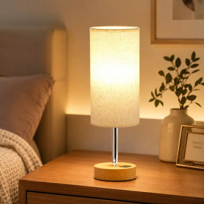 Modern bedside table lamp with USB charging port, 3-way dimmable touch control, linen fabric shade, and wooden base on a bedroom nightstand with warm ambient lighting.