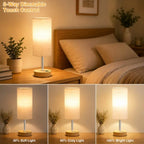 Modern bedside table lamp with USB charging port, 3-way dimmable touch control, linen fabric shade, and wooden base on a bedroom nightstand with warm ambient lighting.
