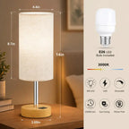 Modern bedside table lamp with USB charging port, 3-way dimmable touch control, linen fabric shade, and wooden base on a bedroom nightstand with warm ambient lighting.