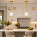 Two modern pendant lights with gold-finished rods and clear ribbed glass shades hanging over a white kitchen island in a bright, contemporary kitchen.