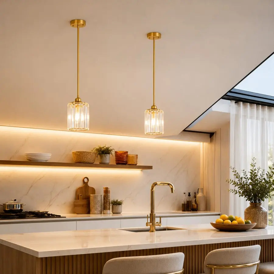 Two modern pendant lights with gold-finished frames and clear glass shades hang over a white marble kitchen island in a bright, contemporary kitchen.