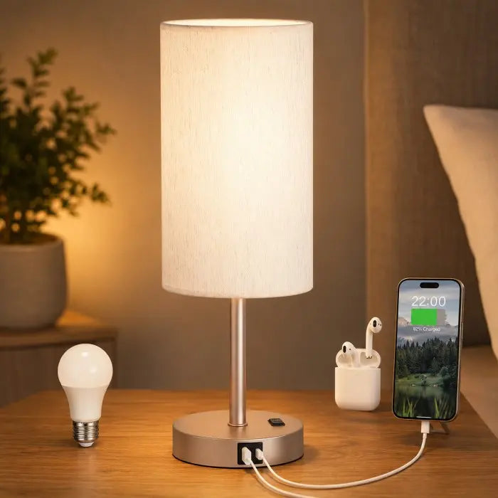 Modern bedside table lamp with USB charging port, 3-way dimmable touch control, linen fabric shade, and wooden base on a bedroom nightstand with warm ambient lighting.
