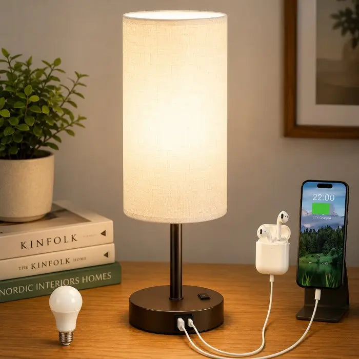 Modern bedside table lamp with USB charging port, 3-way dimmable touch control, linen fabric shade, and wooden base on a bedroom nightstand with warm ambient lighting.