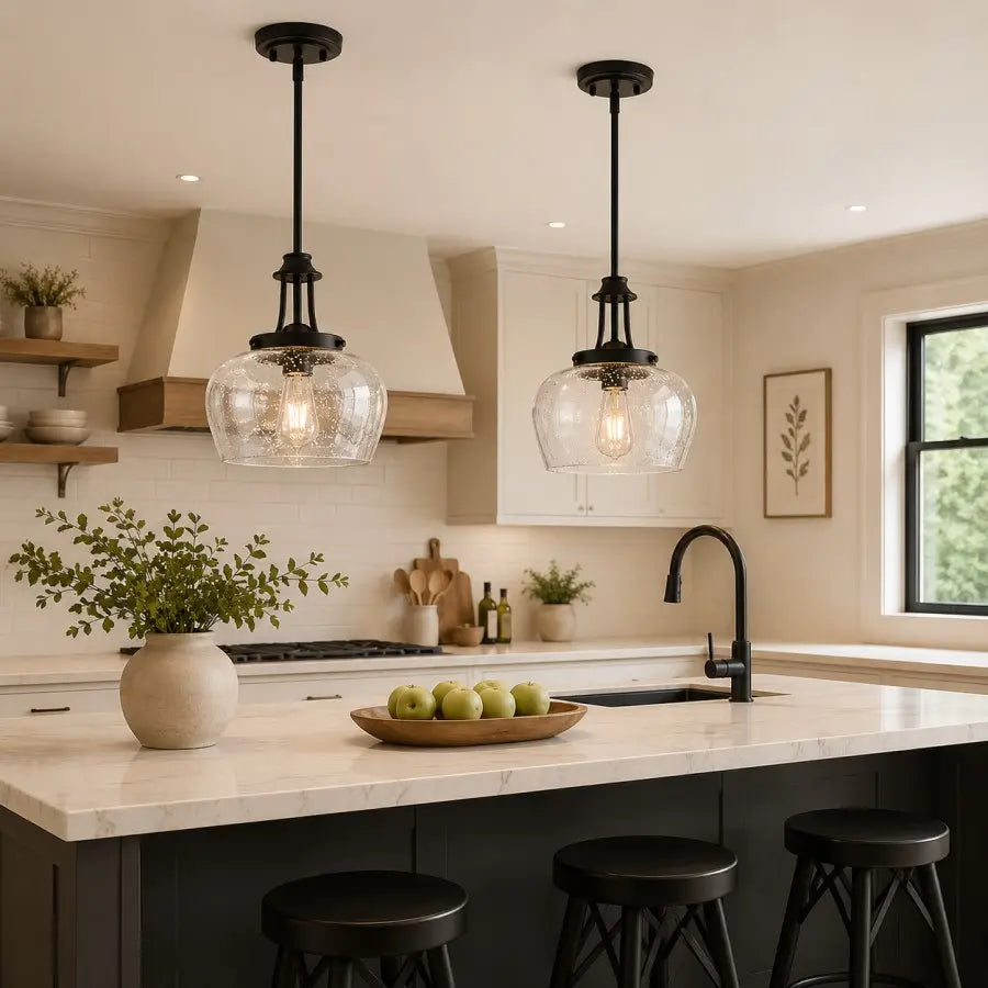 Two black pendant lights with clear glass globes hang over a white marble kitchen island in a modern, warm-toned kitchen.