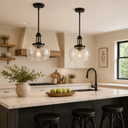 Two black pendant lights with clear glass globes hang over a white marble kitchen island in a modern, warm-toned kitchen.
