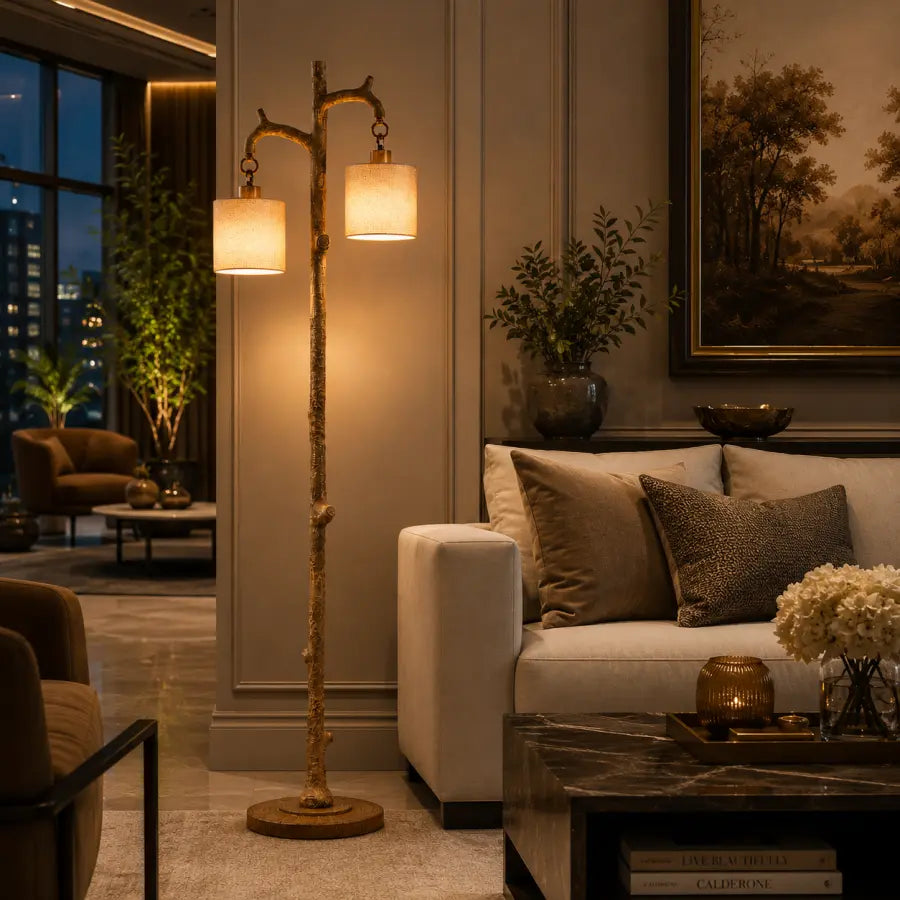 A rustic two-light floor lamp with a branch-like metal frame and warm cream fabric shades, placed in a modern living room next to a white sofa and dark marble coffee table.