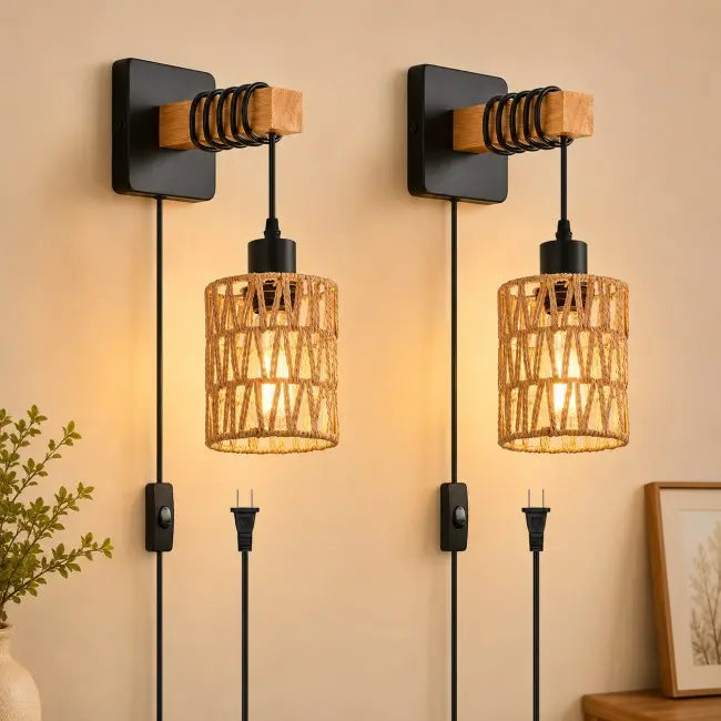 Two matching wall-mounted sconces with black square backplates, wooden accents, spiral wire details, and cylindrical woven rattan shades, shown lit against a beige wall.