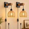 Two matching wall-mounted pendant lights with black metal wall plates, wooden accents, and woven rattan shades, shown lit against a warm beige wall.