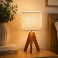 Modern wooden tripod table lamp with linen fabric shade on a bedside table, perfect for bedroom, living room and cozy home lighting