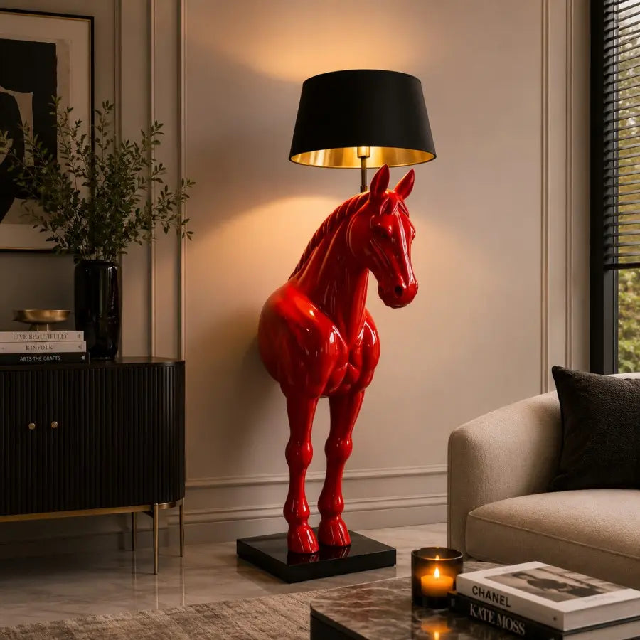 A glossy red horse-shaped table lamp with a black lampshade and gold interior, placed on a black base in a styled living room next to a sofa and sideboard.